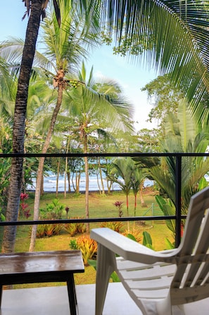 Une vue depuis un balcon, avec une chaise et une table, donnant sur un jardin tropical et l’océan.