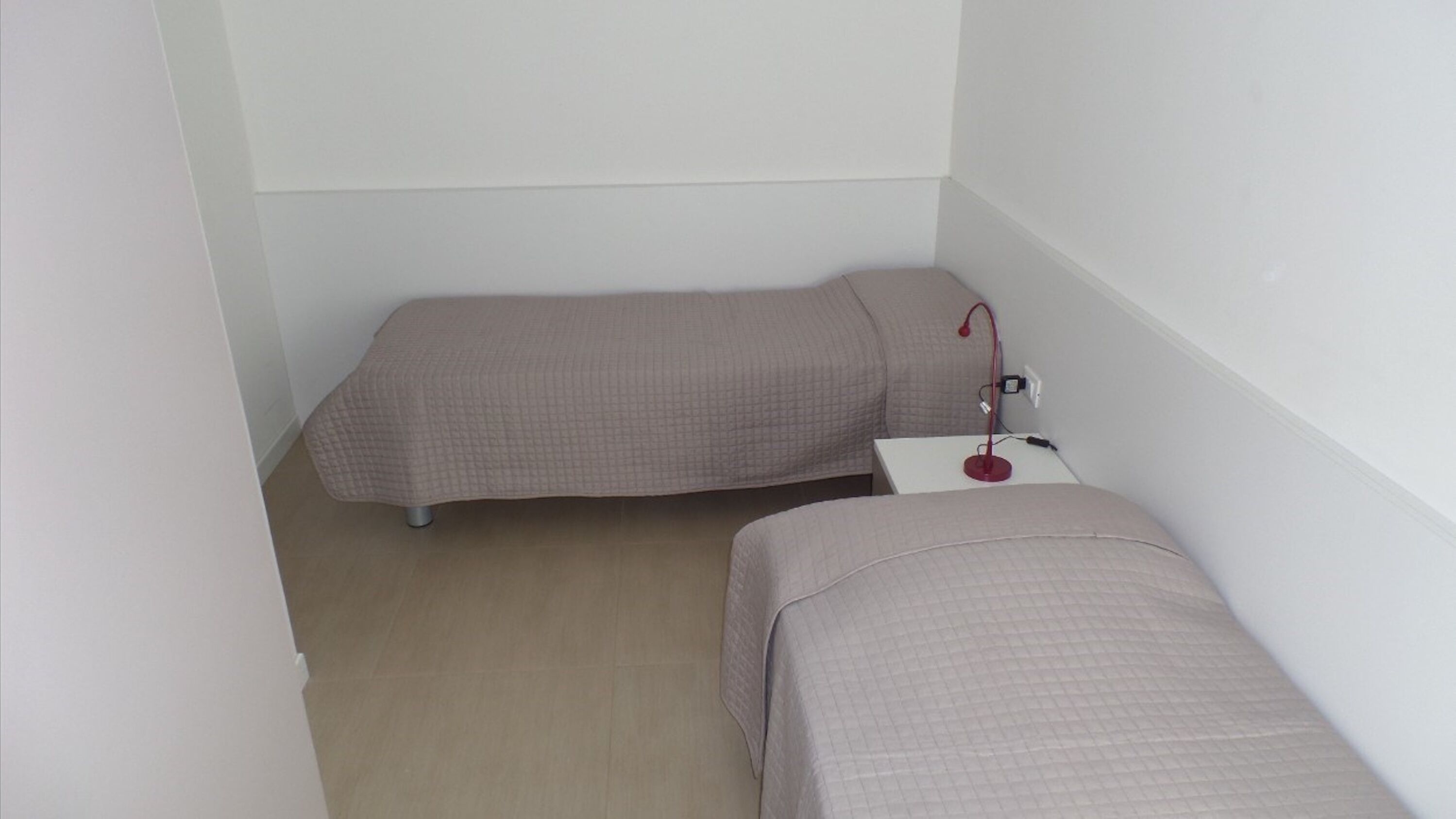 Una habitación pequeña con dos camas, una mesita de noche y una lámpara roja.