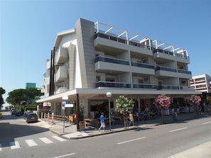 Ein mehrstöckiges Hotel mit Balkonen, einem Café im Erdgeschoss und Sitzgelegenheiten im Freien.