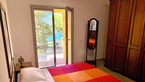 Ein Schlafzimmer mit Bett, Spiegel, Kleiderschrank und einer Glastür zu einem Außenbereich.