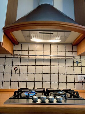 A kitchen with a gas stove, a vent hood, and a tiled backsplash. - In relaxation looking at the sea, with pool (Finale Ligure)