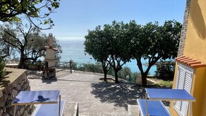Eine Terrasse mit zwei Tischtennisplatten, einem gepflasterten Weg und Blick aufs Meer.