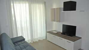A modern living room with a sofa, TV, and cabinets. - Coastal Apartment With Spacious Terrace (San Michele al Tagliamento)