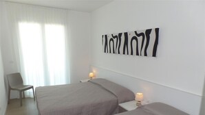 A hotel room with two beds, a chair, and a wall-mounted artwork. - Coastal Apartment With Spacious Terrace (San Michele al Tagliamento)