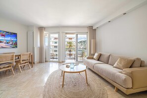 Ein Wohnzimmer mit einer Couch, einem runden Couchtisch, einem Esstisch mit Stühlen und Blick durch Glastüren auf einen Balkon.