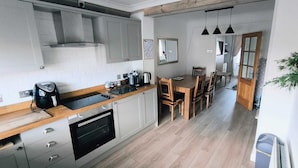 A modern kitchen with a built-in oven, a coffee maker, and wooden chairs at a dining table.