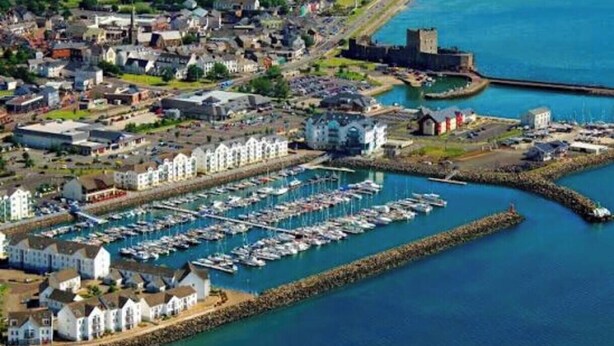 An aerial view of a coastal town with a marina, historic buildings, and a castle.