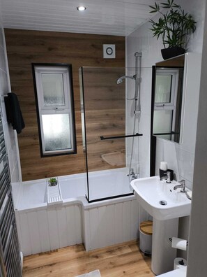 A modern bathroom with a glass shower enclosure, a white sink, and a wooden floor.