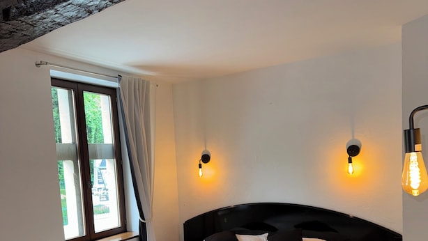 Un dormitorio con una cama, dos lámparas de pared, un ventanal con cortinas y una alfombra roja.