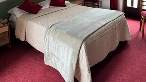 Una habitación de hotel con una cama, una silla, una mesita de noche, una lámpara de pared y una ventana con cortinas.