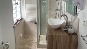 Un baño moderno con ducha envuelta en vidrio, un lavamanos blanco y un mueble de tocador de madera.