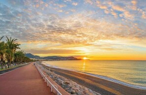 A coastal sunset view with a paved walkway, palm trees, and a calm sea. - Apt 4 guests Promenade des Anglais (Nice)