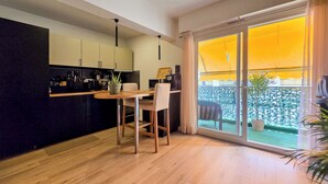 A modern kitchen with a dining area, large sliding glass doors, and a view of a garden. - Apt 4 guests Promenade des Anglais (Nice)