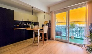 A modern kitchen with a dining area, large sliding glass doors, and a view of a garden. - Apt 4 guests Promenade des Anglais (Nice)