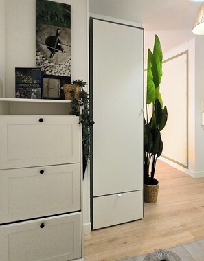 A modern room with a white wardrobe, a small shelf with decorative items, and a large green plant. - Apt 4 guests Promenade des Anglais (Nice)