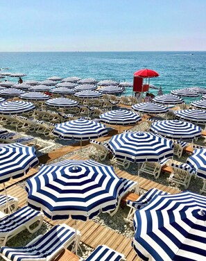 A beach with numerous striped umbrellas and lounge chairs. - Apt 4 guests Promenade des Anglais (Nice)