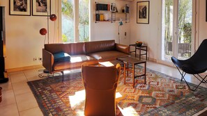 Ein Wohnzimmer mit einem braunen Ledersofa, einem gemusterten Teppich, einem schwarzen Sessel und einem Bücherregal mit Büchern und Dekoration.