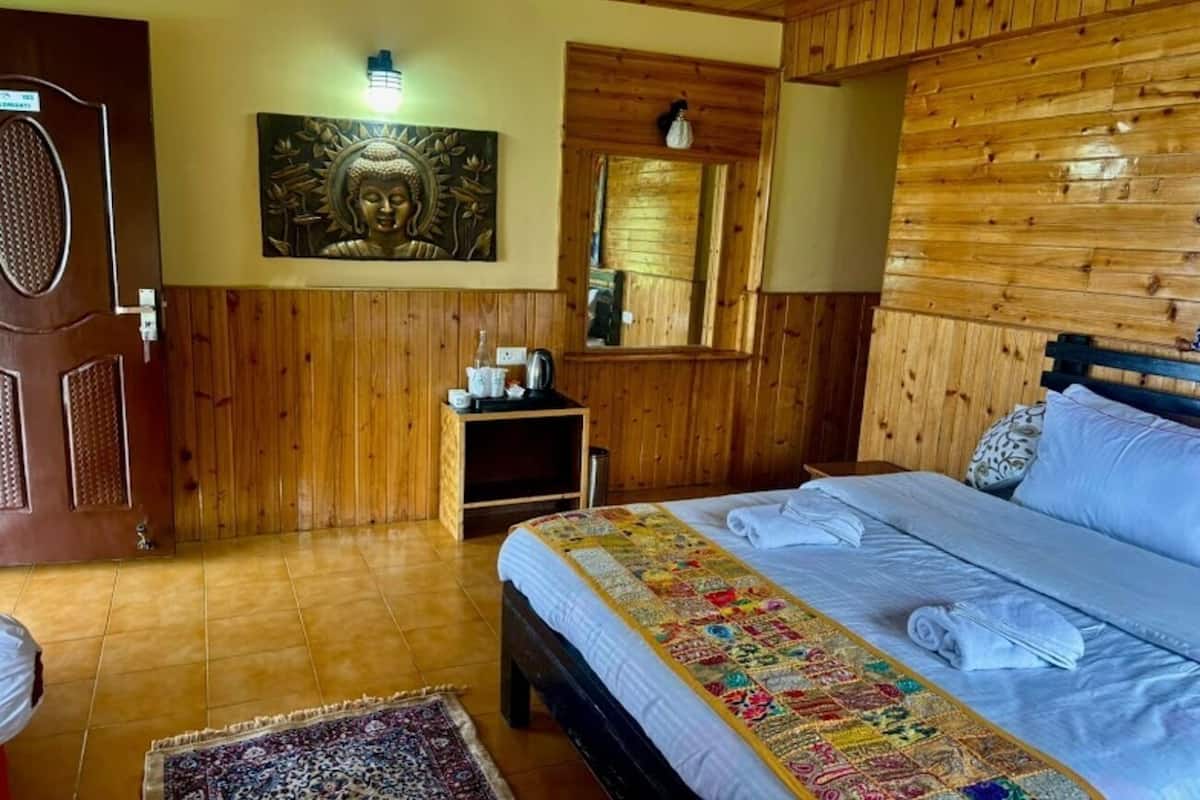 A wooden-paneled room with a bed, a small table, a chair, and a wall-mounted Buddha statue.