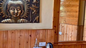 A wooden paneled wall with a Buddha painting, a small table with a kettle, cups, and a bottle.