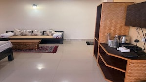A room with a bed, a wooden bench, a small table with kitchen items, and a wall-mounted TV.
