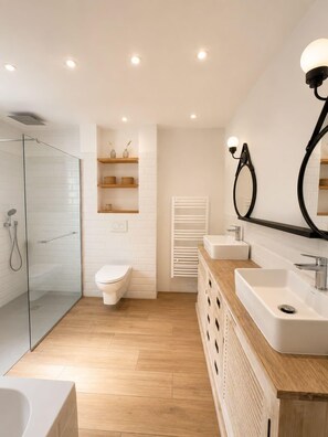 Et moderne badeværelse med glasvæg omkring brusenichen, toilet, vaskebord med spejl og indbyggede hylder.