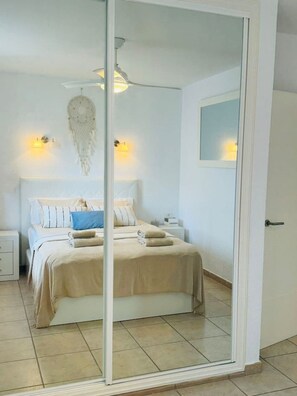 Ein Schlafzimmer mit einem Bett, Nachttischen, einem an der Wand hängenden Traumfänger und einem Spiegel.