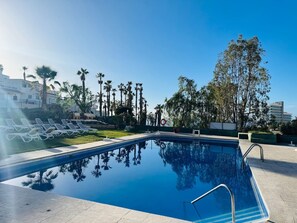 Ein Swimmingpool mit Liegestühlen, umgeben von Palmen und einem klaren Himmel.