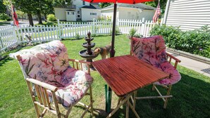 Eine Terrasse mit zwei Holzstühlen, einem Tisch, einem roten Sonnenschirm und einem kleinen Brunnen.