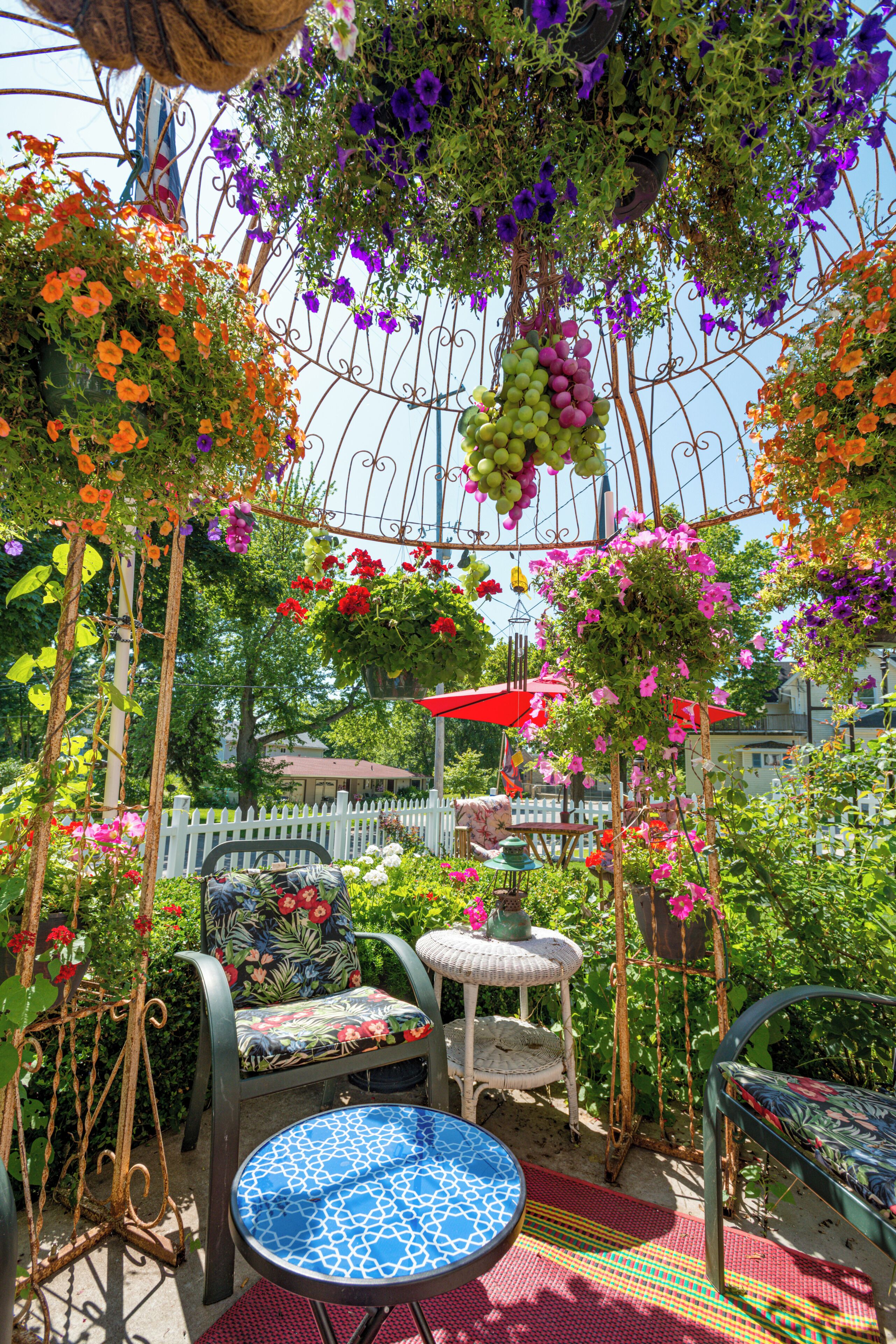 An outdoor seating area with a round table and chairs, surrounded by lush greenery and flowering plants.
