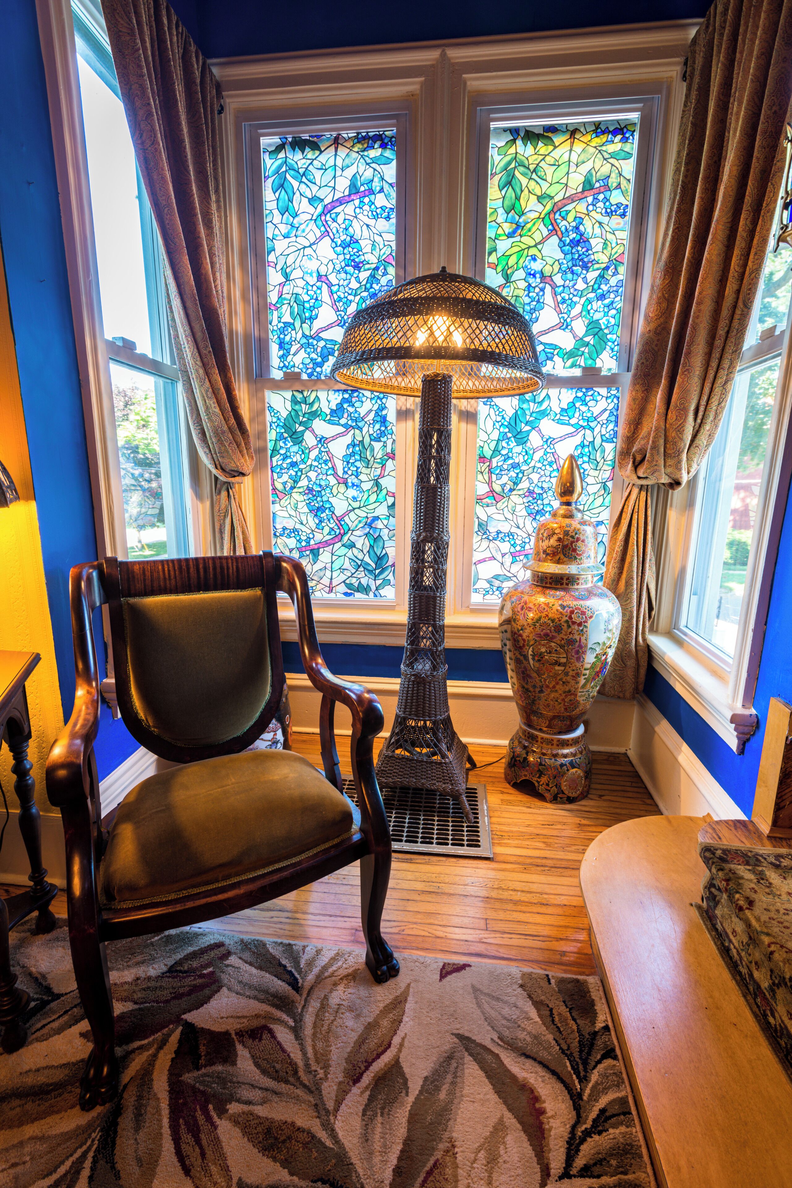 A room with a large stained glass window, a floor lamp, a chair, and a decorative vase.