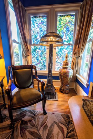 A room with a large stained glass window, a floor lamp, a chair, and a decorative vase.
