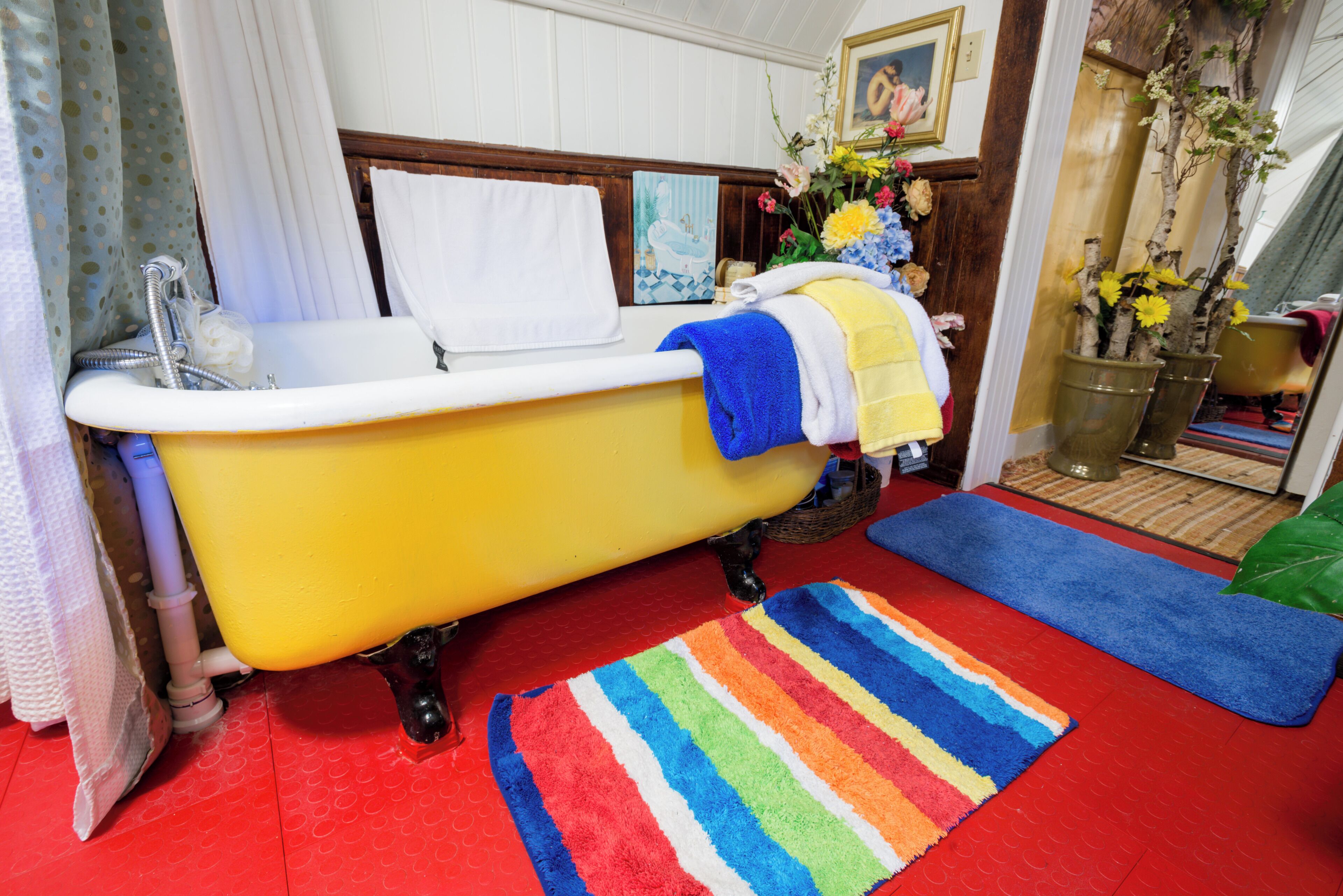 A bathroom with a yellow bathtub, a striped rug, and a vase of flowers.