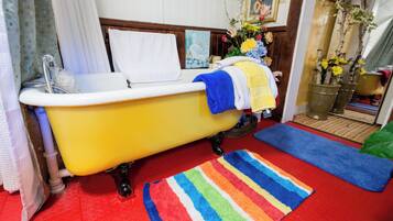 A bathroom with a yellow bathtub, a striped rug, and a vase of flowers.