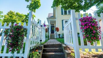 A house with a white picket fence, a brick pathway leading to the front door, and hanging flower baskets.