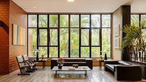 A spacious lobby with a large window, a sofa, a coffee table, and a brick wall. - Flat Premium Bounganville  Al. Grajau (Barueri)