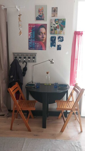 A room with a table, two wooden chairs, a lamp, a bottle, and various wall art. - Fully-equipped furnished studio - Malakoff, ideal for training/professional assignment, 3 weeks min. (Malakoff)
