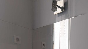 Un baño con un lavamanos blanco, un espejo, un estante con un recipiente de vidrio y un perchero para toallas.