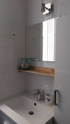 A bathroom with a white sink, a mirror, a shelf with a glass container, and a towel rack. - Fully-equipped furnished studio - Malakoff, ideal for training/professional assignment, 3 weeks min. (Malakoff)
