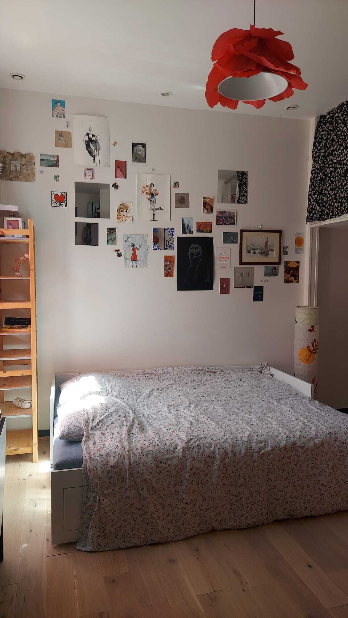 A bedroom with a bed, wooden floor, and a wall decorated with various pictures.