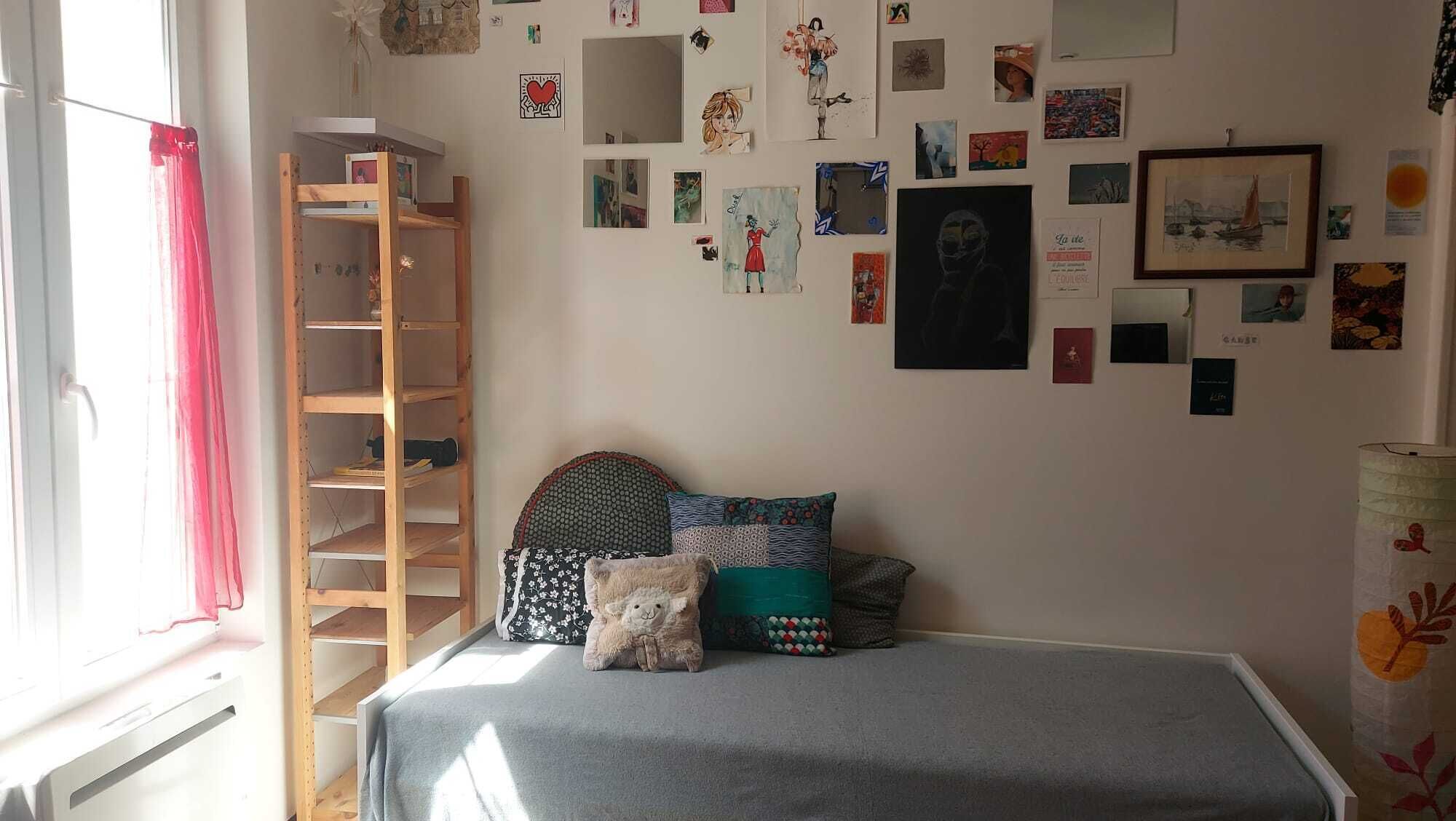 Un dormitorio con una cama litera, una escalera de madera, una pared decorada con diversas obras de arte y una ventana con cortinas rojas.