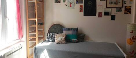 Un dormitorio con una cama litera, una escalera de madera, una pared decorada con diversas obras de arte y una ventana con cortinas rojas.