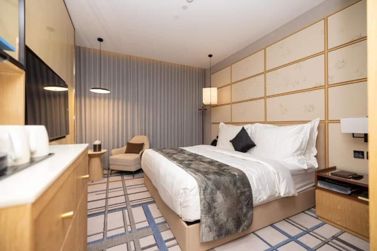 A hotel room with a bed, bedside table, chair, and a large mirror.