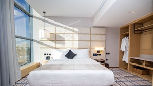 A modern hotel room with a large bed, a bedside table, a wardrobe, and a view through a large window. - 7Crown Tahliah Hotel (Riyadh)