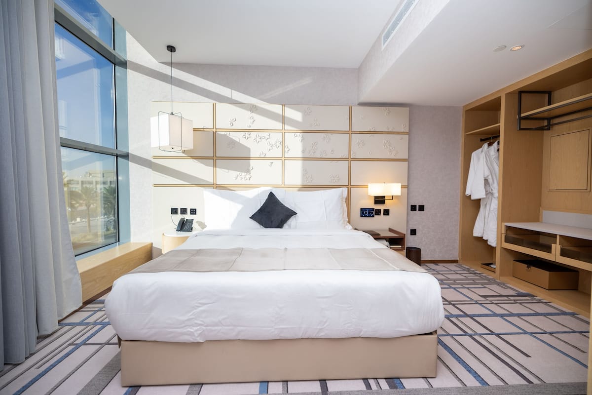 Una habitación de hotel moderna con una cama grande, una mesita de noche, un armario y vistas a través de un ventanal.