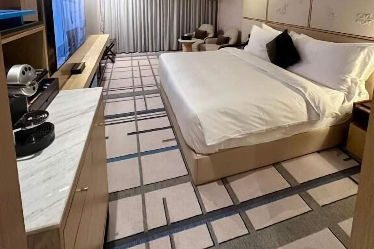 A hotel room with a bed, a desk with a computer, a TV, a lamp, and a curtain.