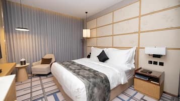 Een hotelkamer met een bed, nachtkastje, stoel en een groot raam met gordijnen.