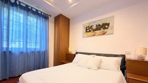 Een hotelkamer met een bed, nachtkastje, lamp, schilderij aan de muur en raam met gordijnen.