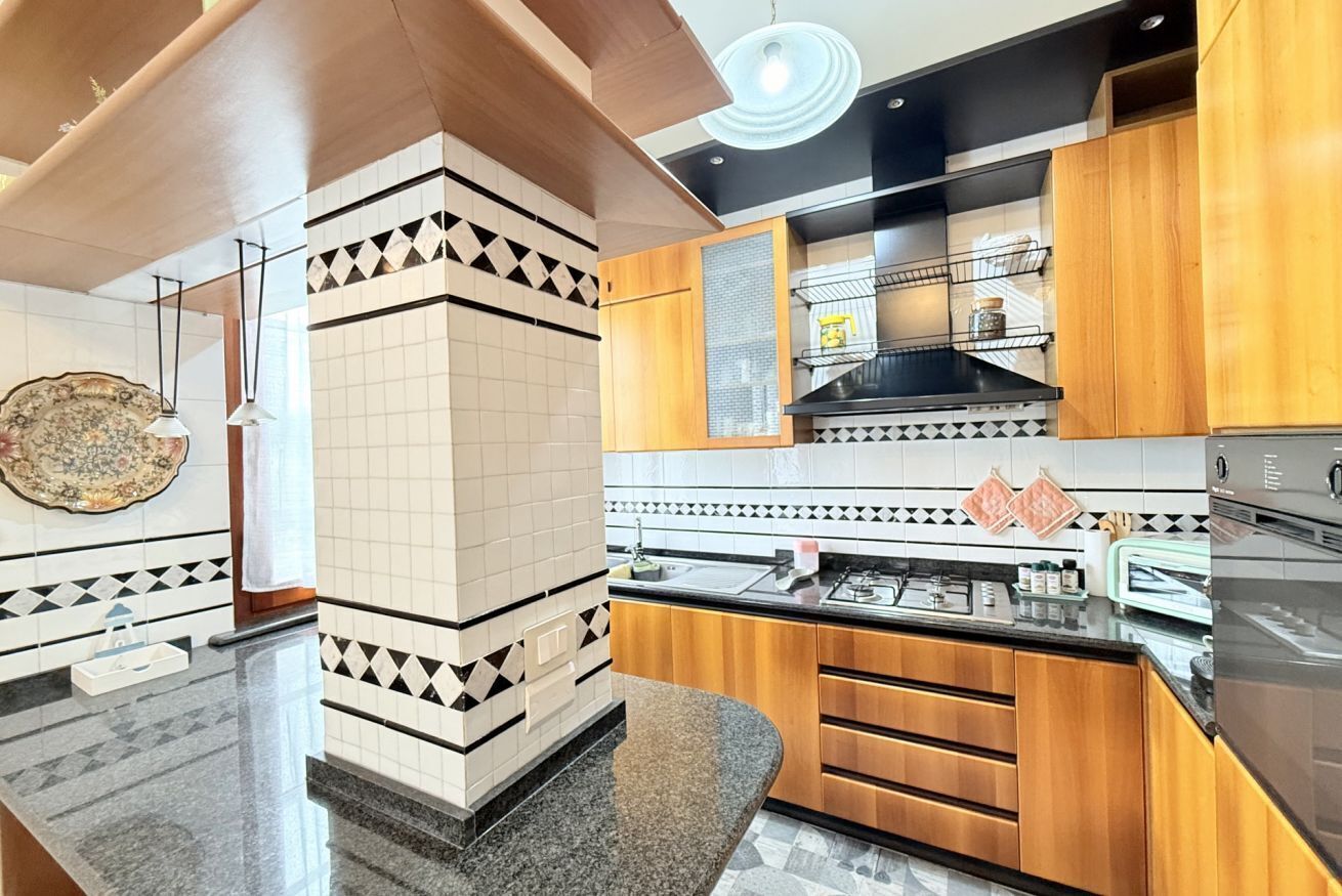 A modern kitchen with a black countertop, wooden cabinets, a black stove, and a patterned backsplash.