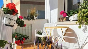 A balcony with white wicker chairs, a small round table, and various potted plants. - Cosy aparment 200 meters from the beach (Vilanova i la Geltrú)