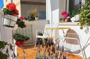 Ein Balkon mit weißen Korbstühlen, einem kleinen runden Tisch und verschiedenen Blumentöpfen.